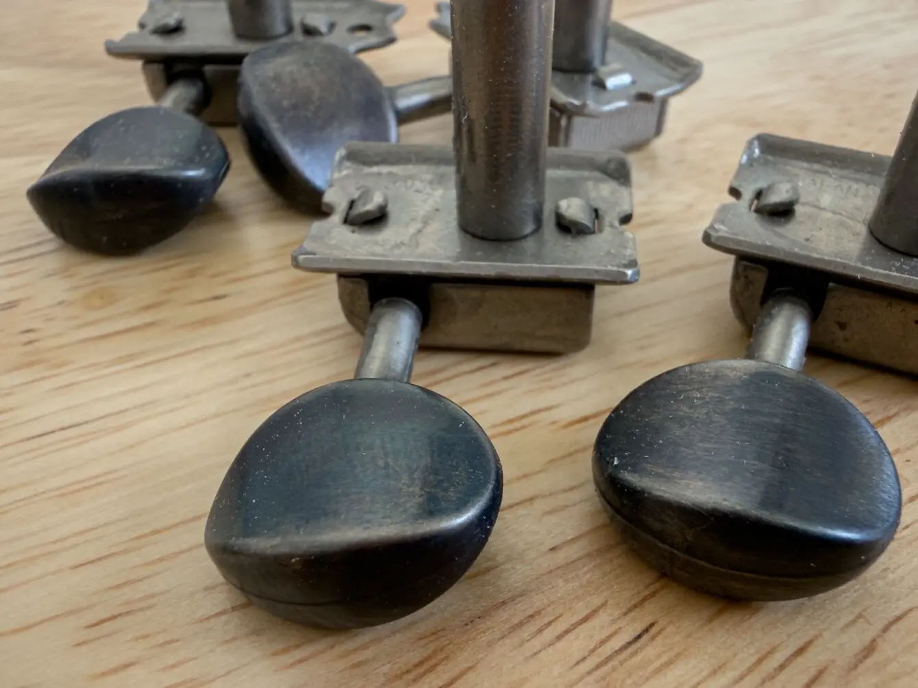 Vintage oval guitar tuners with blackened metal buttons on a workshop bench, showing the hand-worked finish before installation.