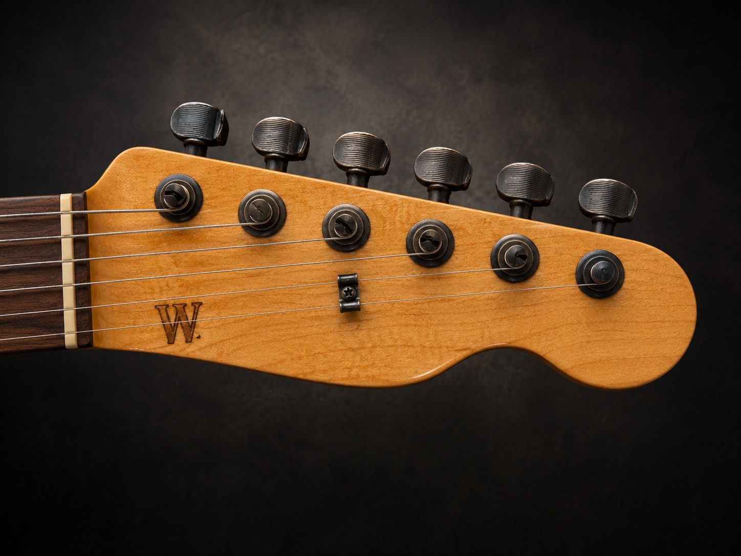 Wimberly headstock, small burned W in Tru-Oil-finished maple with blackened vintage oval tuners against a dark backdrop.