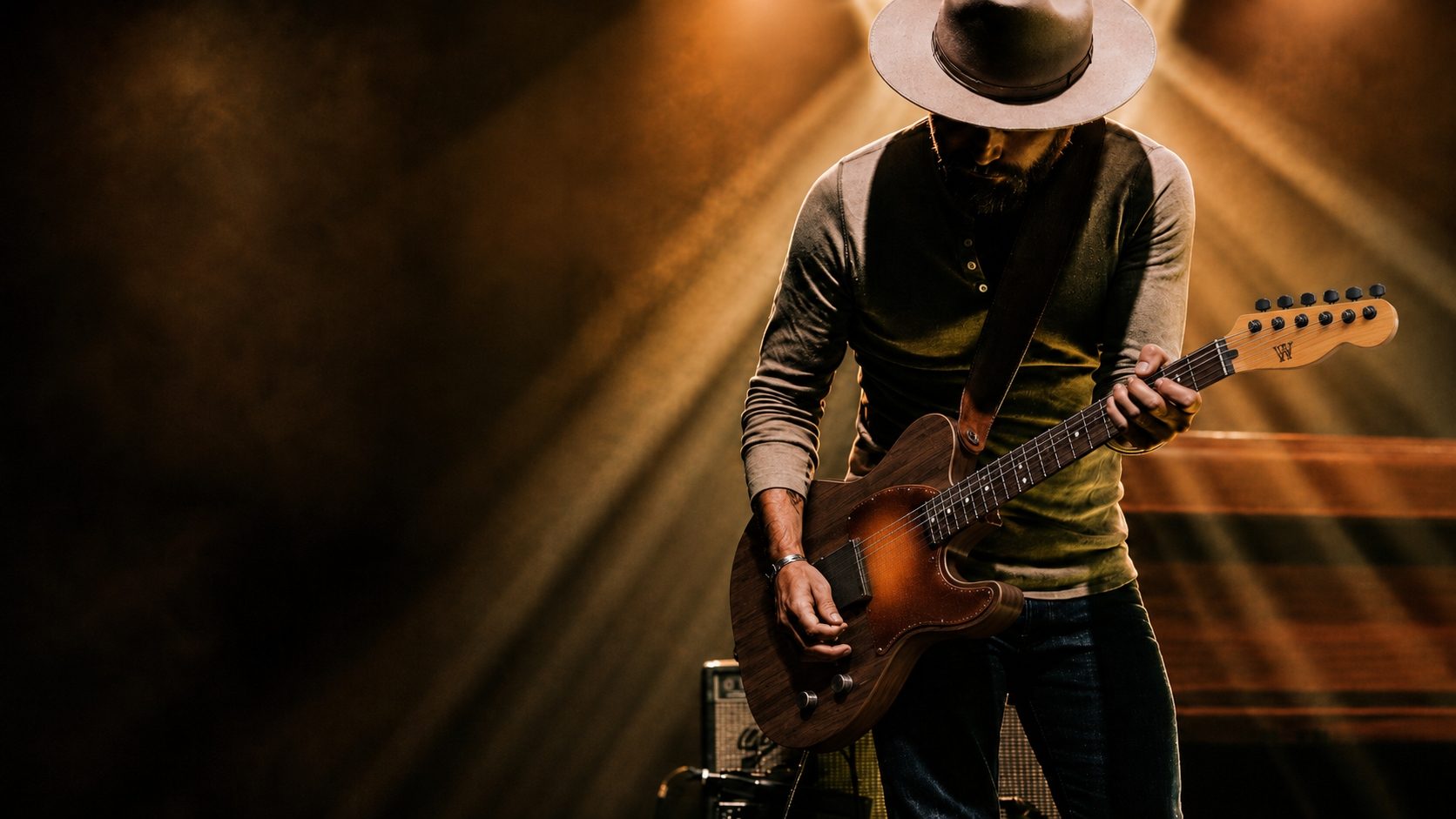 Preston Wimberly playing a Wimberly guitar on stage, warm stage light, wide-brim hat, W maker's mark visible on the headstock.